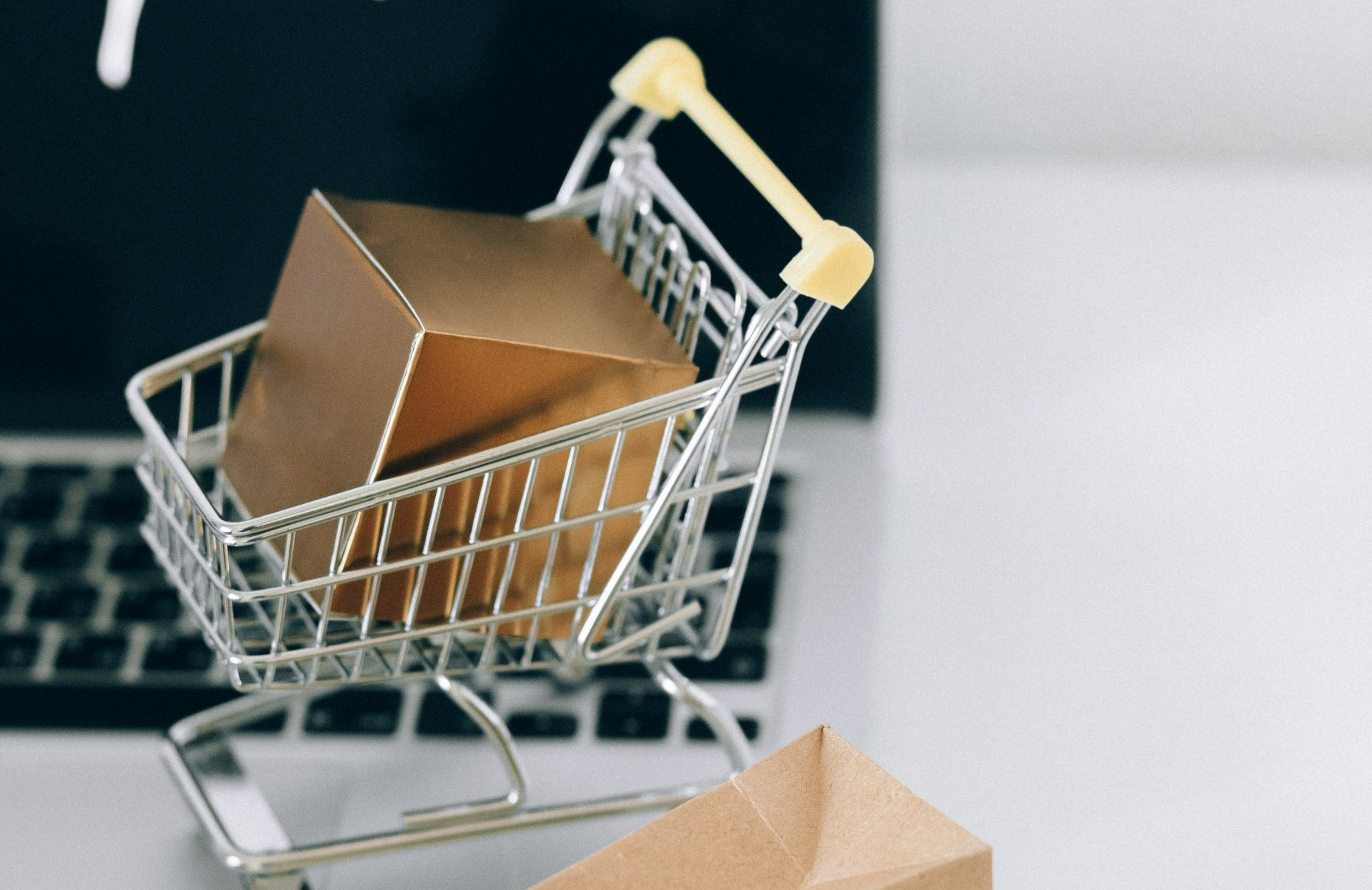 Small shopping cart with a gold box on a laptop keyboard, suggesting online shopping.