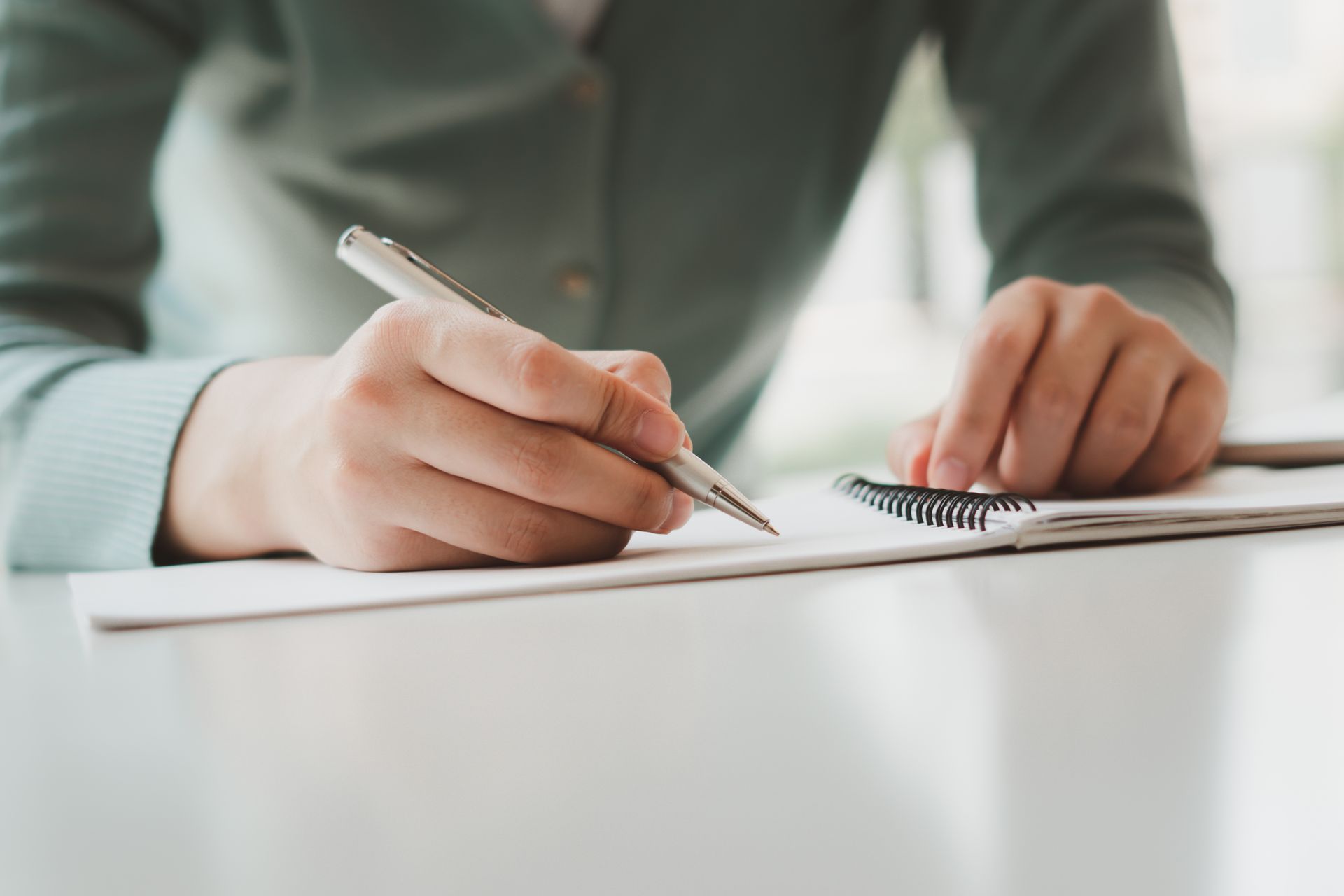 Hand writing in a notebook on a desk with a pen, close-up view