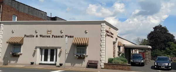Front view of a funeral home building with awnings and parked cars under a cloudy sky