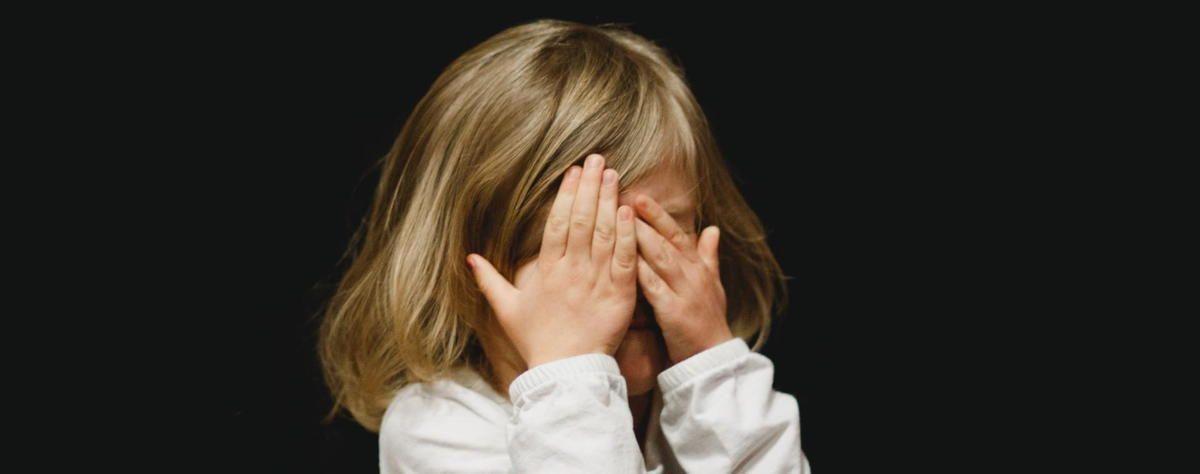 A little girl is covering her face with her hands on a black background. A little girl is covering her face with her hands on a black background.