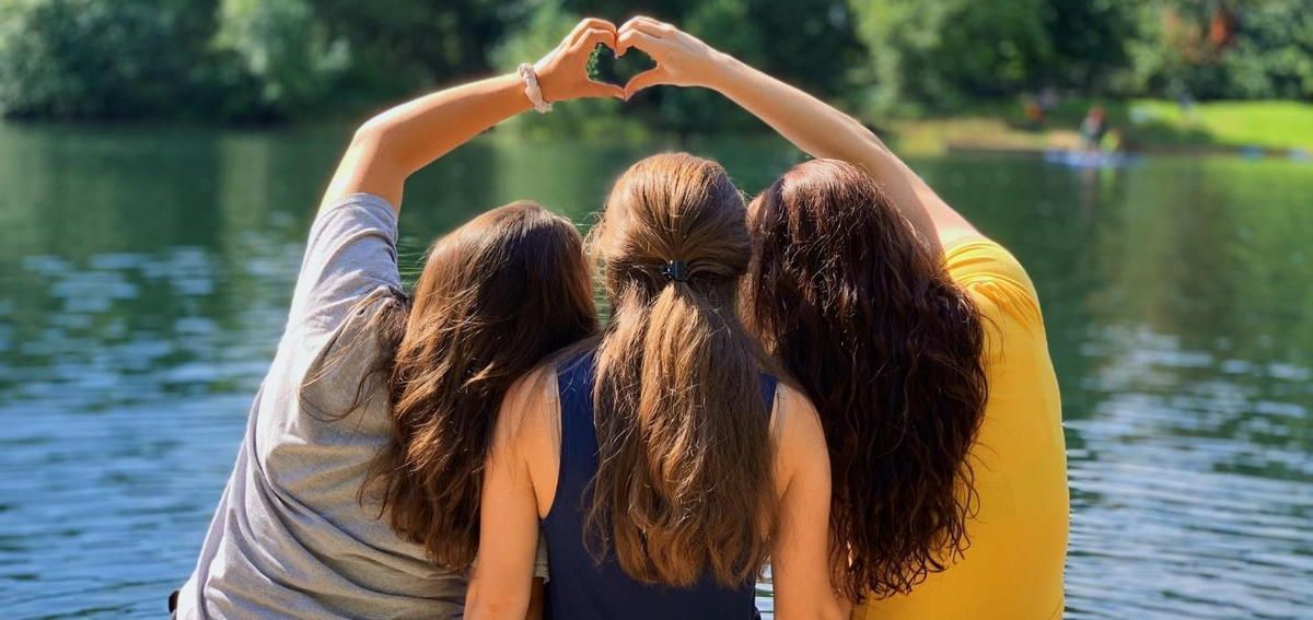 Three women are making a heart shape with their hands in front of a lake. Three women are making a heart shape with their hands in front of a lake.