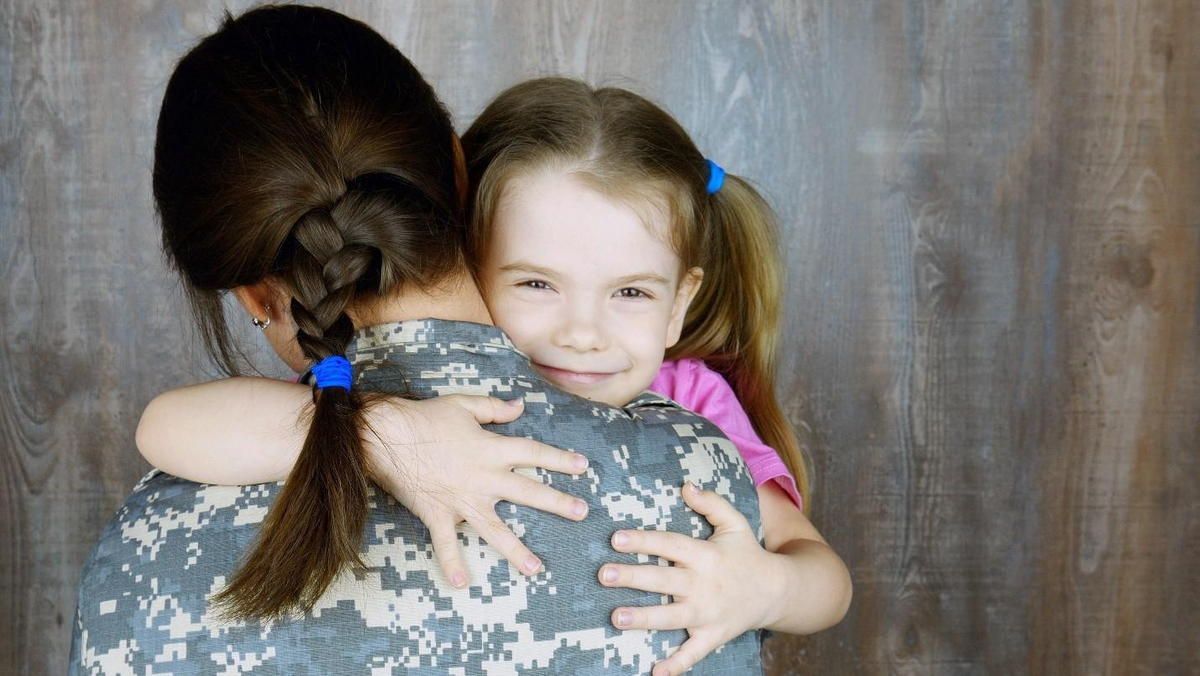 A woman in a military uniform is hugging a little girl. A woman in a military uniform is hugging a little girl.