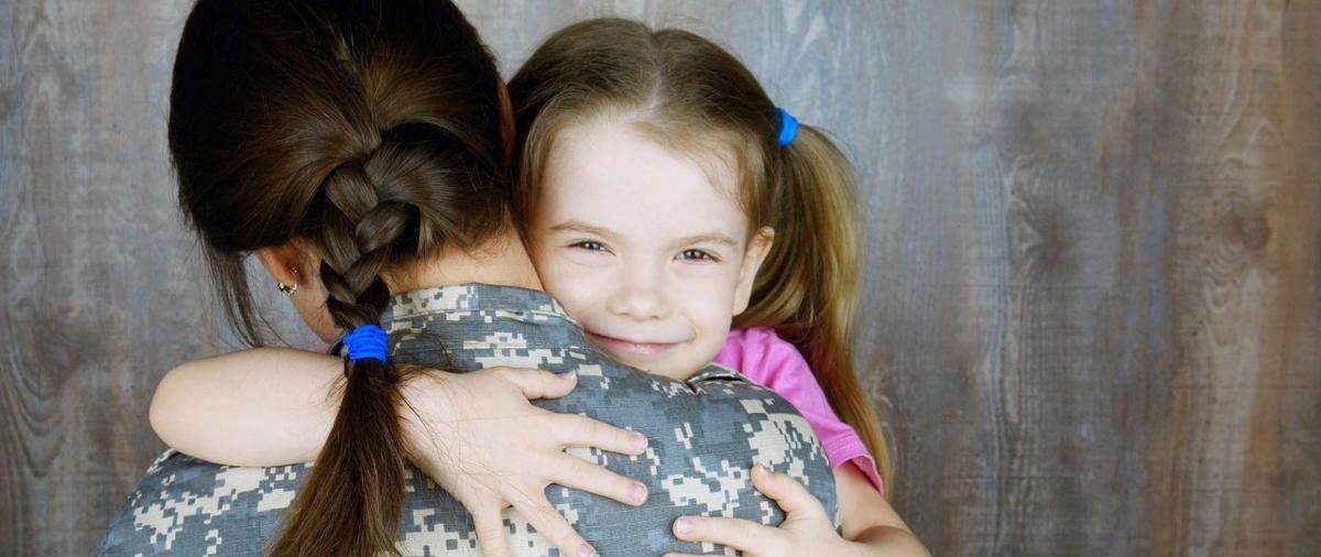 A woman in a military uniform is hugging a little girl. A woman in a military uniform is hugging a little girl.