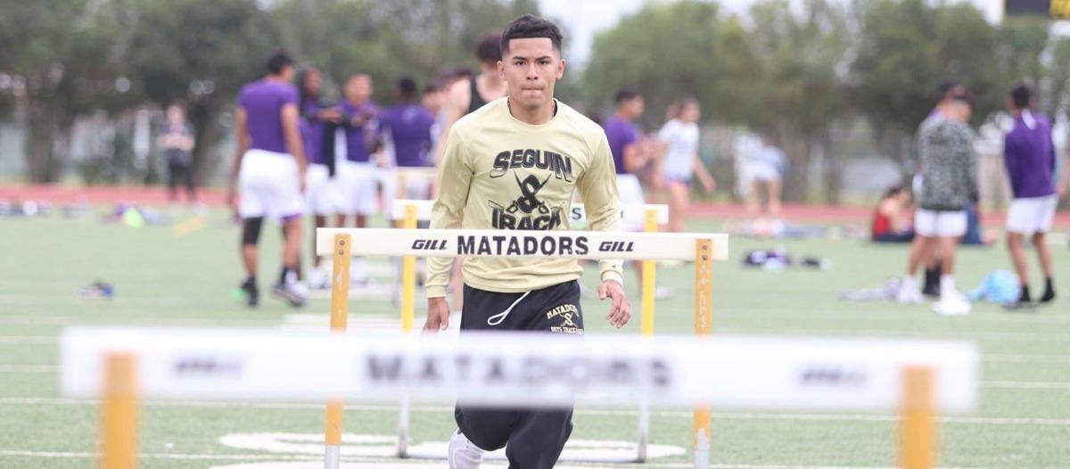 A man in a matadors shirt is jumping over hurdles on a field. A man in a matadors shirt is jumping over hurdles on a field.