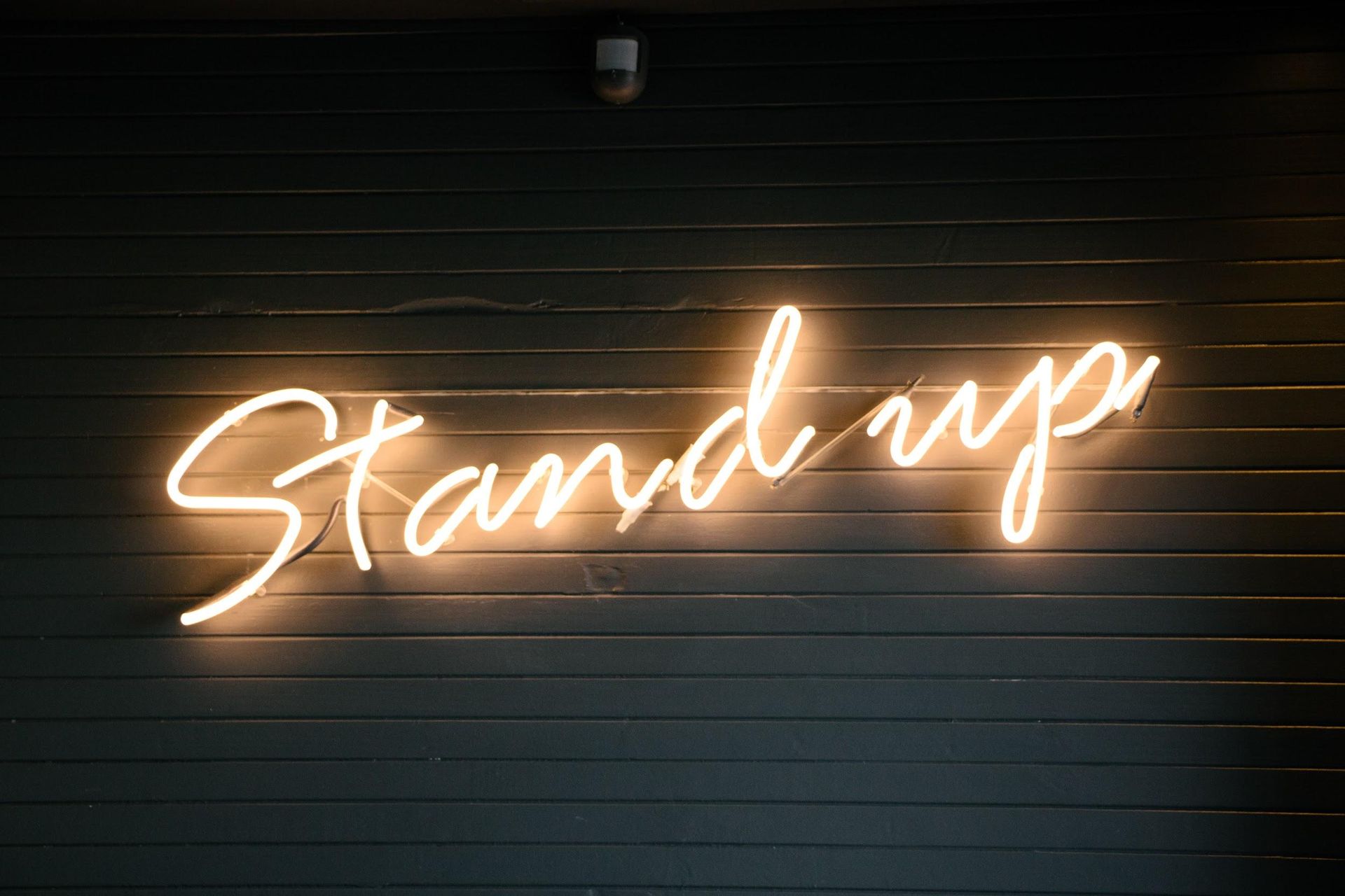 A neon sign that says `` stand up '' is lit up on a wall.