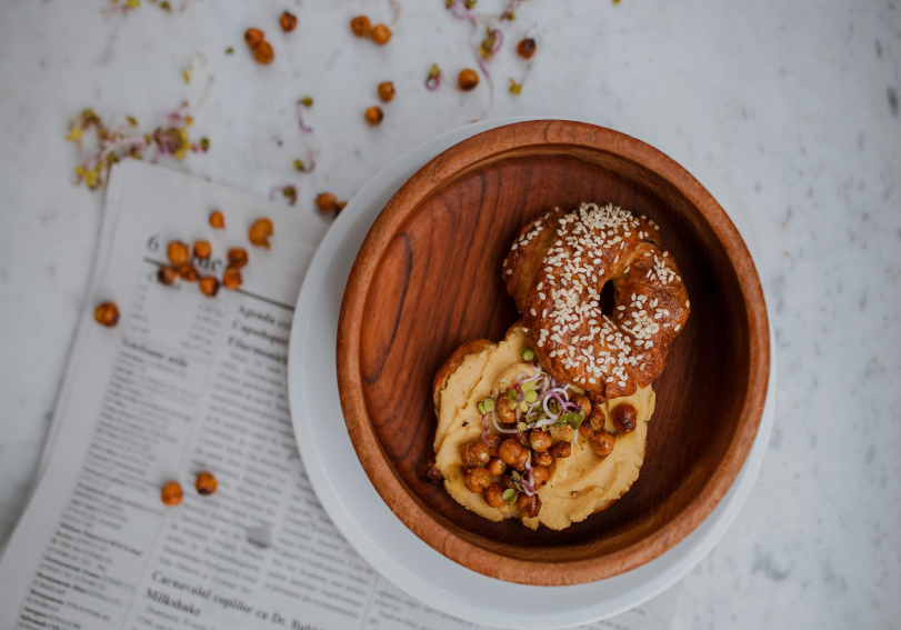 A wooden bowl filled with donuts and hummus is sitting on top of a newspaper.