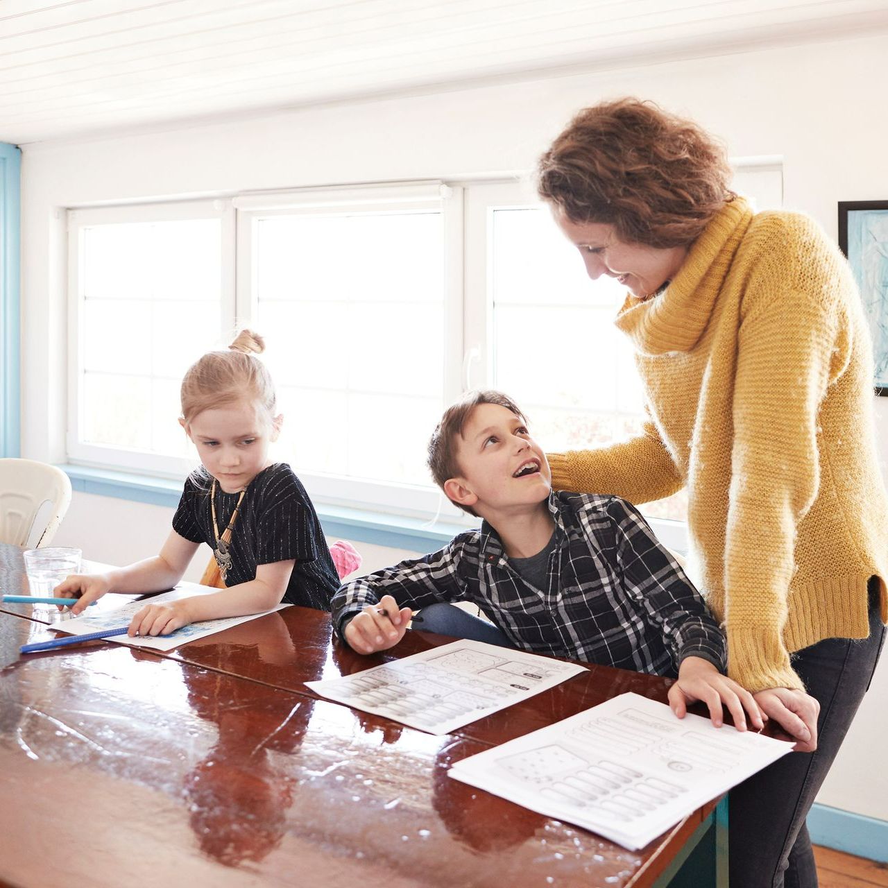 A woman in a yellow sweater is helping two children with their homework A woman in a yellow sweater is helping two children with their homework