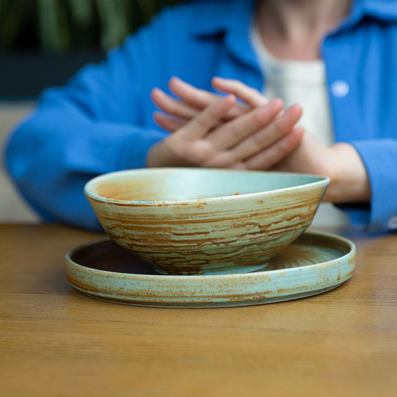 A woman in a blue jacket is sitting at a table with a bowl and plate A woman in a blue jacket is sitting at a table with a bowl and plate