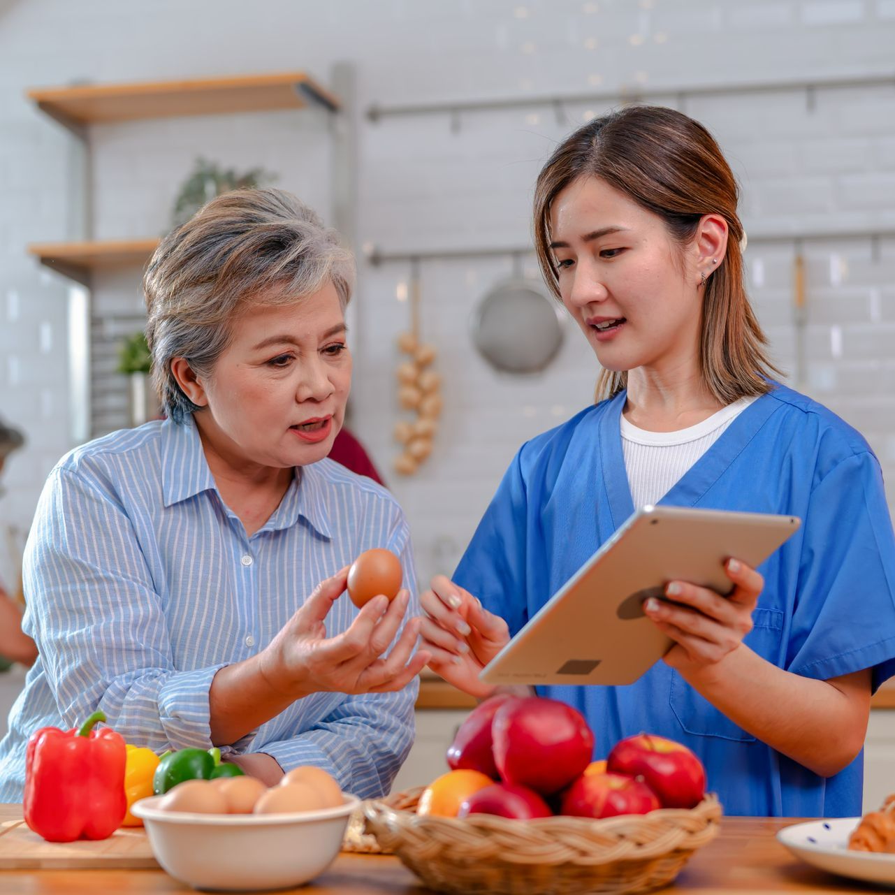 A nurse is showing an older woman how to cook on a tablet. A nurse is showing an older woman how to cook on a tablet.