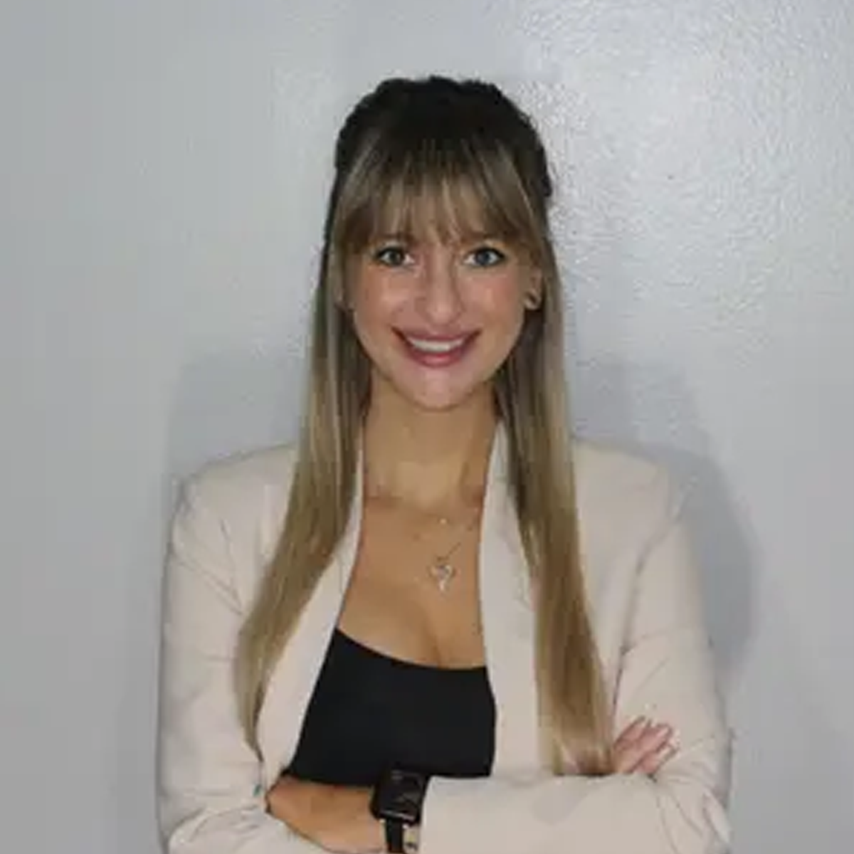 A woman in a white jacket and black top is standing with her arms crossed and smiling. A woman in a white jacket and black top is standing with her arms crossed and smiling.