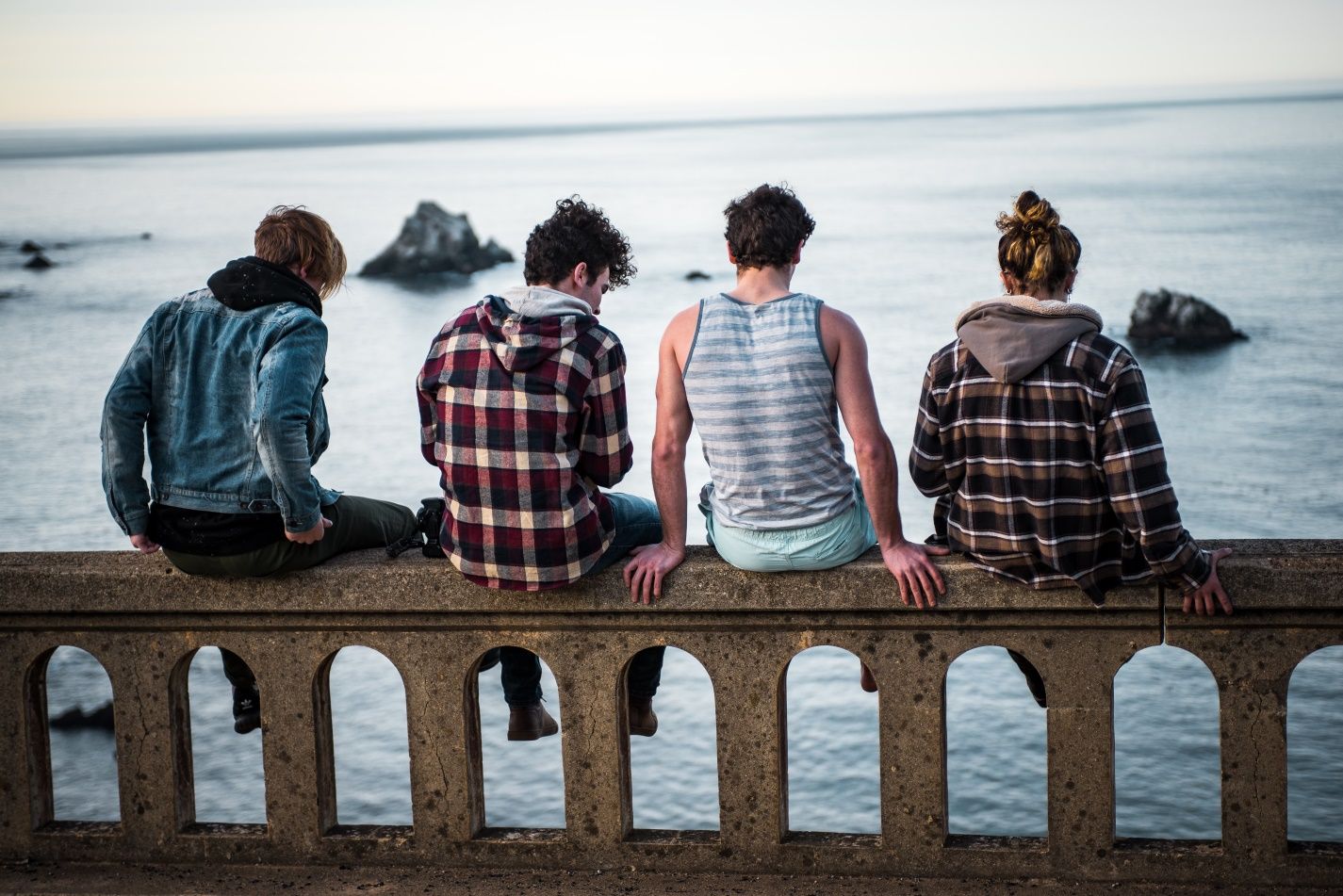 A group of people are sitting on a ledge overlooking the ocean. A group of people are sitting on a ledge overlooking the ocean.