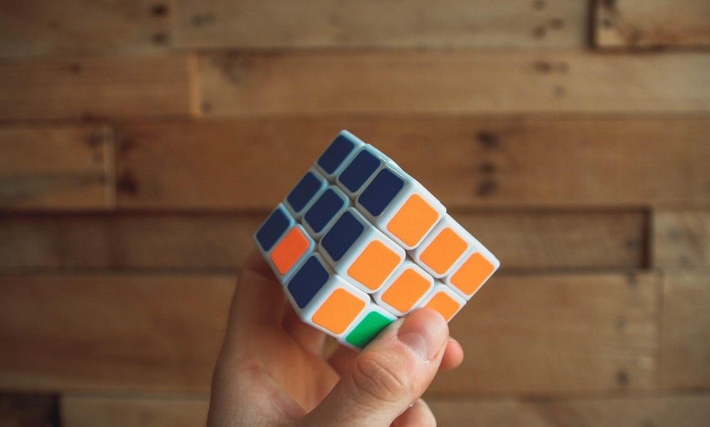 A person is holding a rubik 's cube in their hand in front of a wooden wall. A person is holding a rubik 's cube in their hand in front of a wooden wall.