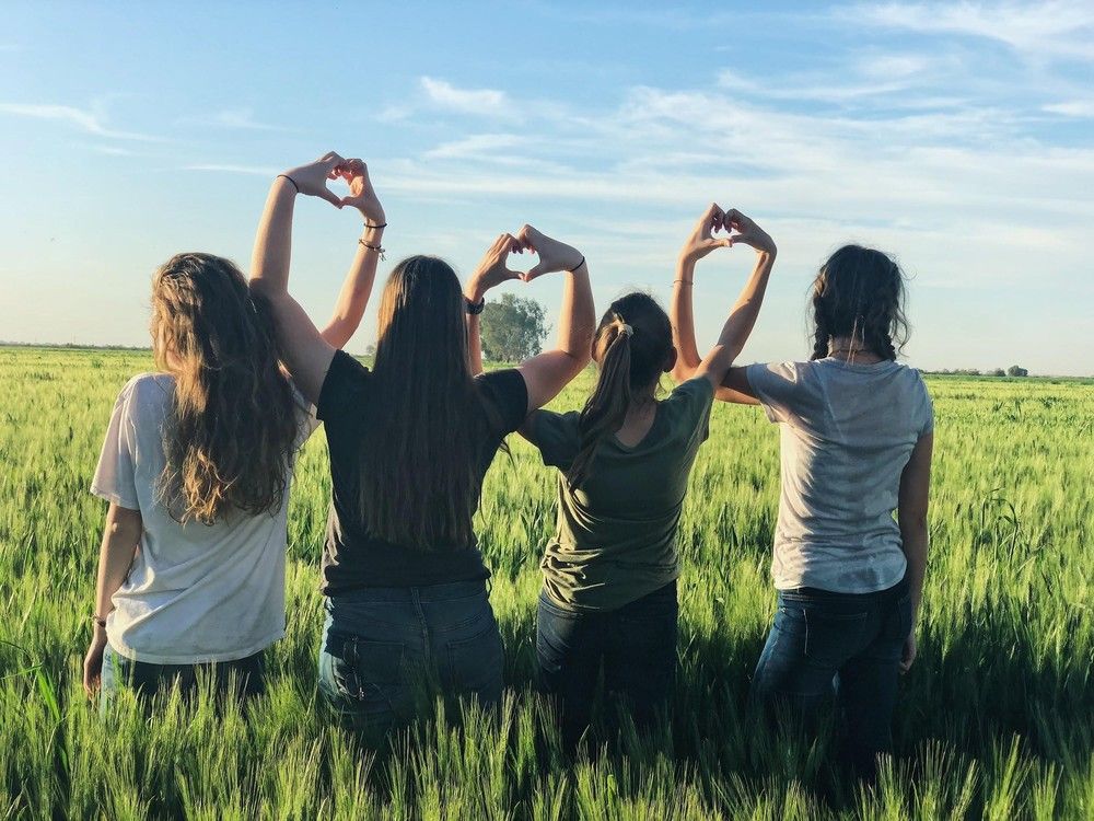 A group of girls are making a heart shape with their hands in a field. A group of girls are making a heart shape with their hands in a field.