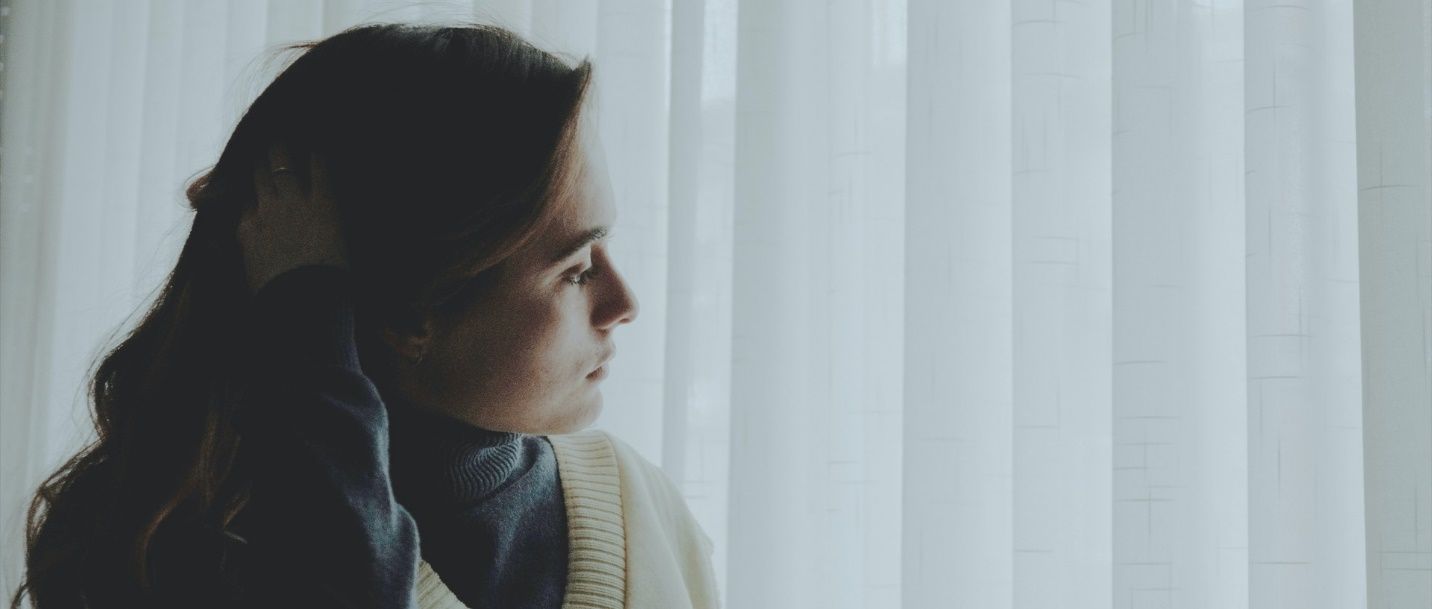 A woman is standing in front of a window looking out. A woman is standing in front of a window looking out.