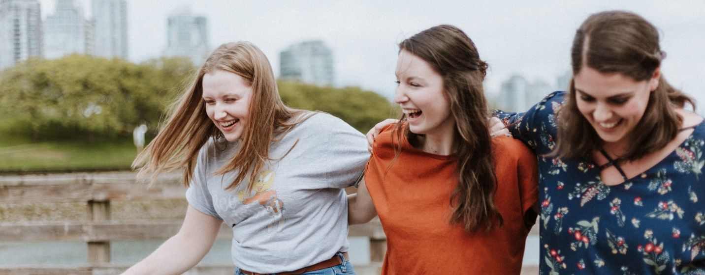 Three young women are standing next to each other and laughing. Three young women are standing next to each other and laughing.