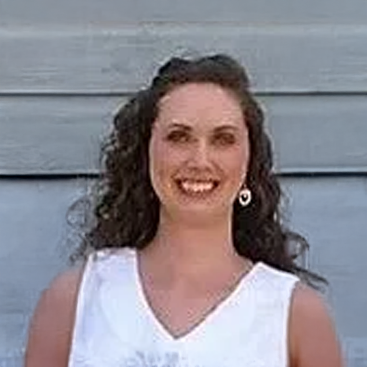 A woman wearing a white tank top and earrings is smiling for the camera. A woman wearing a white tank top and earrings is smiling for the camera.