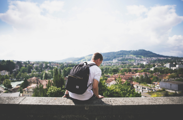 A man with a backpack is sitting on a wall overlooking a city. A man with a backpack is sitting on a wall overlooking a city.