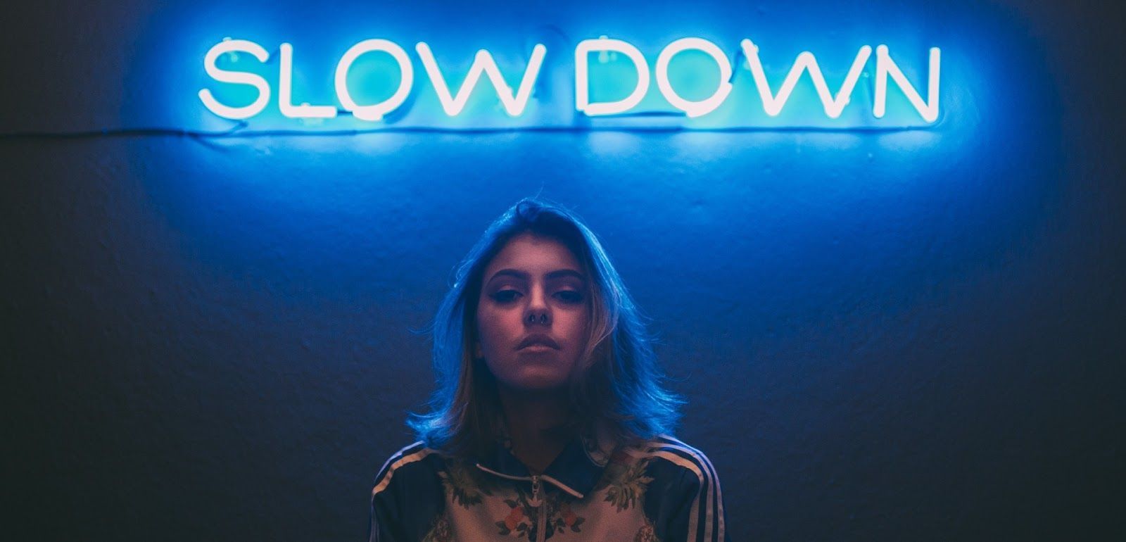 A woman is standing in front of a neon sign that says slow down.