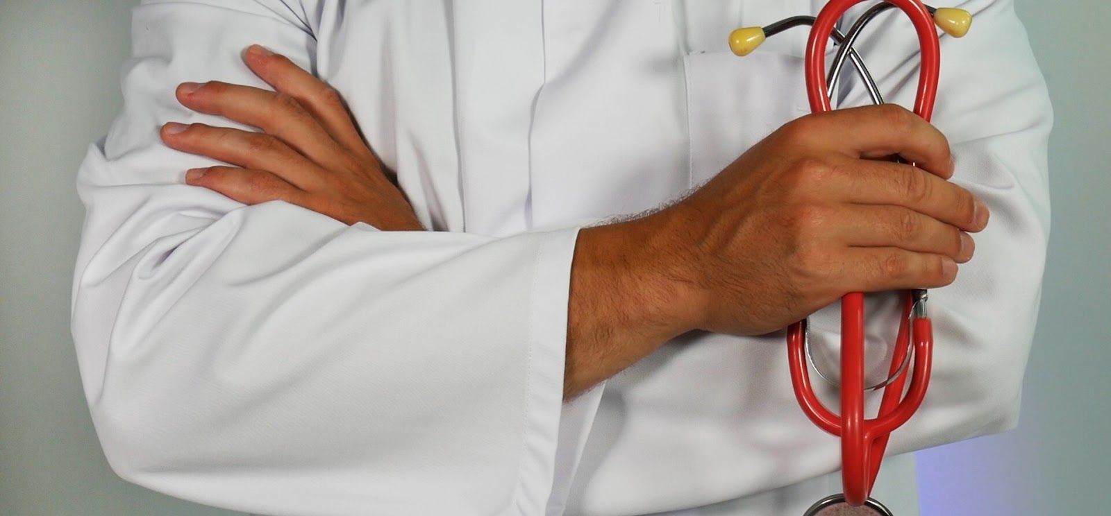 A doctor is holding a red stethoscope with his arms crossed. A doctor is holding a red stethoscope with his arms crossed.