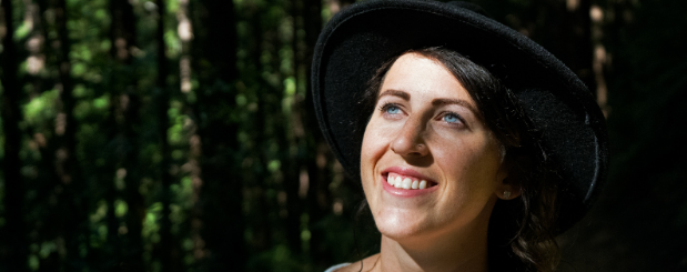 A woman wearing a black hat is smiling in the woods. A woman wearing a black hat is smiling in the woods.