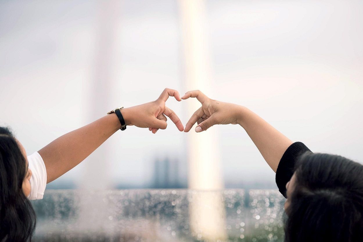 Two women are making a heart shape with their hands in front of a fountain. Two women are making a heart shape with their hands in front of a fountain.