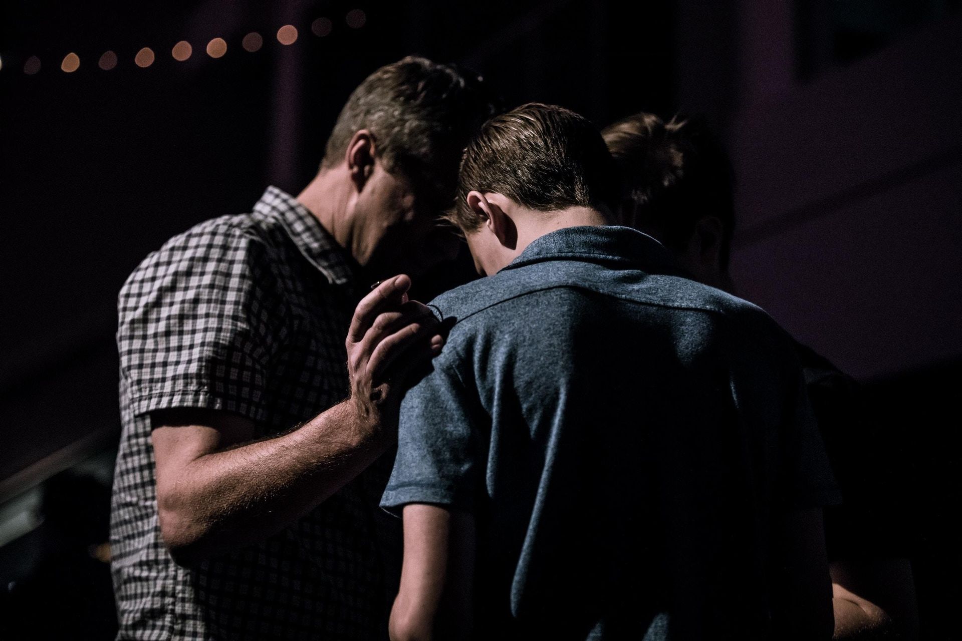 Two men are praying together in a dark room. Two men are praying together in a dark room.