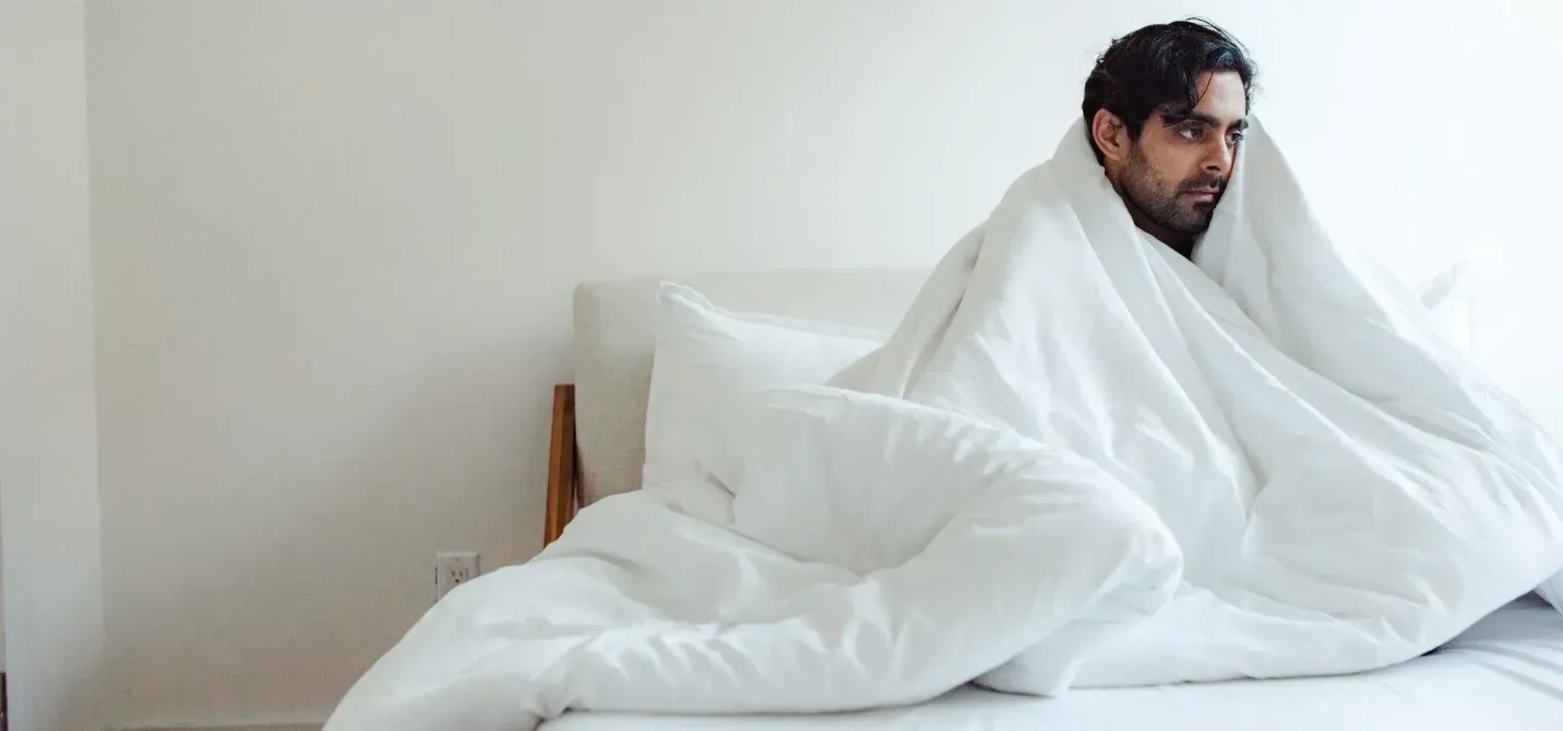 A man is sitting on a bed wrapped in a white blanket. A man is sitting on a bed wrapped in a white blanket.