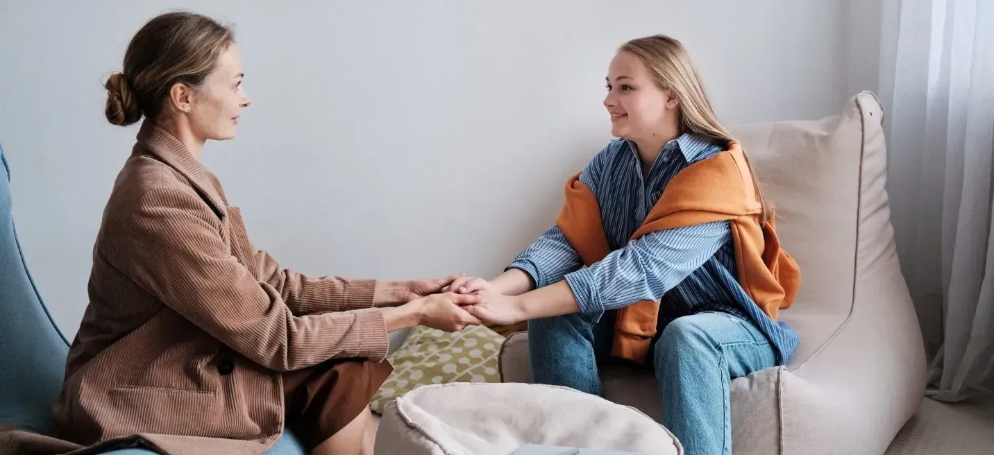 A woman is holding a woman 's hand while sitting on a couch. A woman is holding a woman 's hand while sitting on a couch.