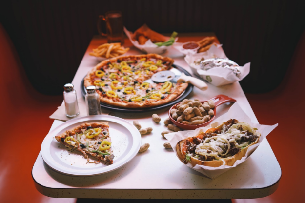 A table topped with plates of food including a pizza and a hot dog