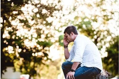 A man is sitting on a rock with his head in his hands.