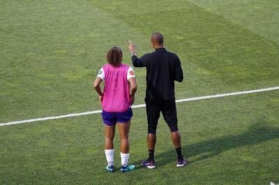 A man and a woman are standing on a soccer field talking to each other.