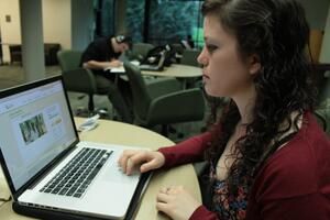 A woman is sitting at a table using a laptop computer.