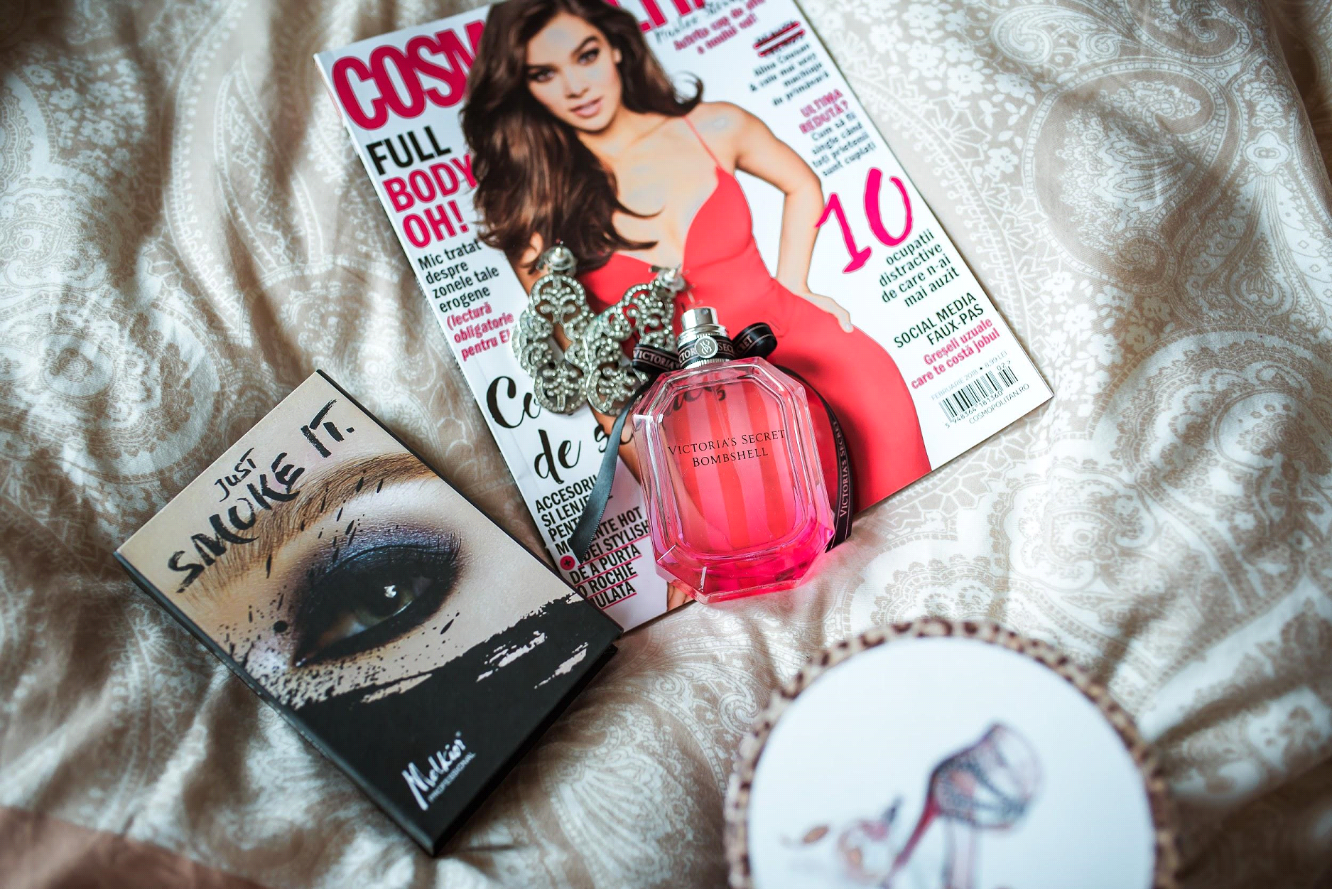 A bottle of perfume is sitting on top of a magazine on a bed. A bottle of perfume is sitting on top of a magazine on a bed.