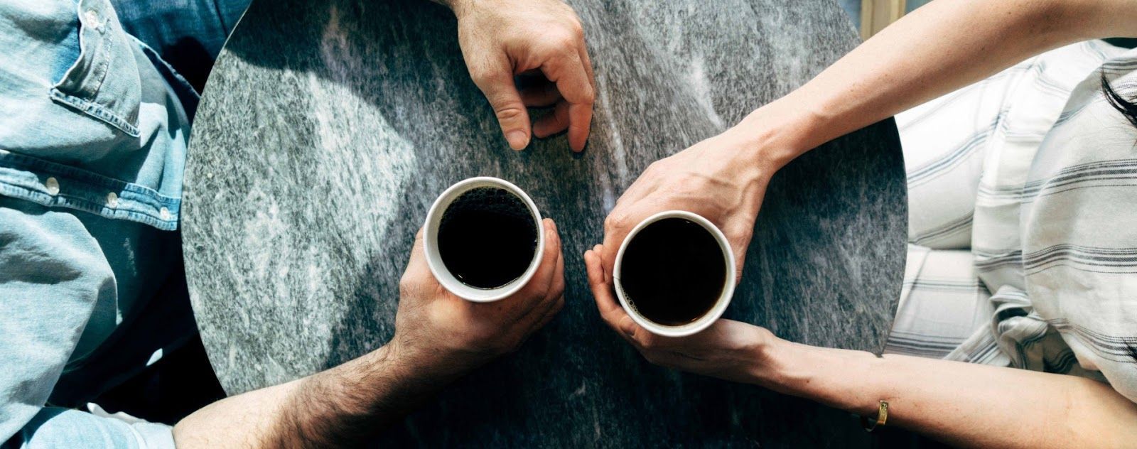 Two people are sitting at a table holding cups of coffee.