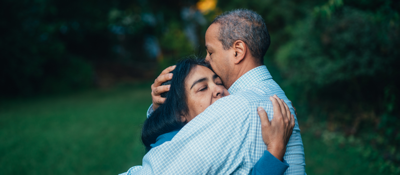 A man and a woman are hugging each other in a park.