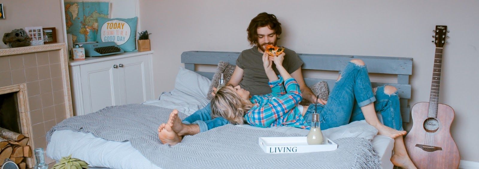 A man and a woman are laying on a bed eating pizza.