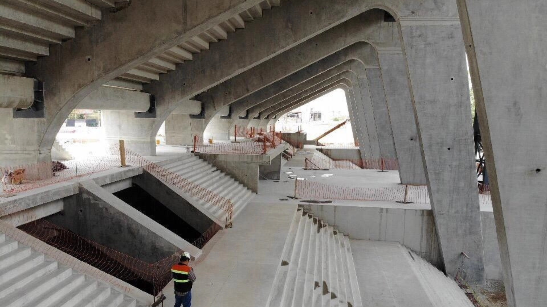 Concrete stadium under construction; worker stands below tiers of seating.