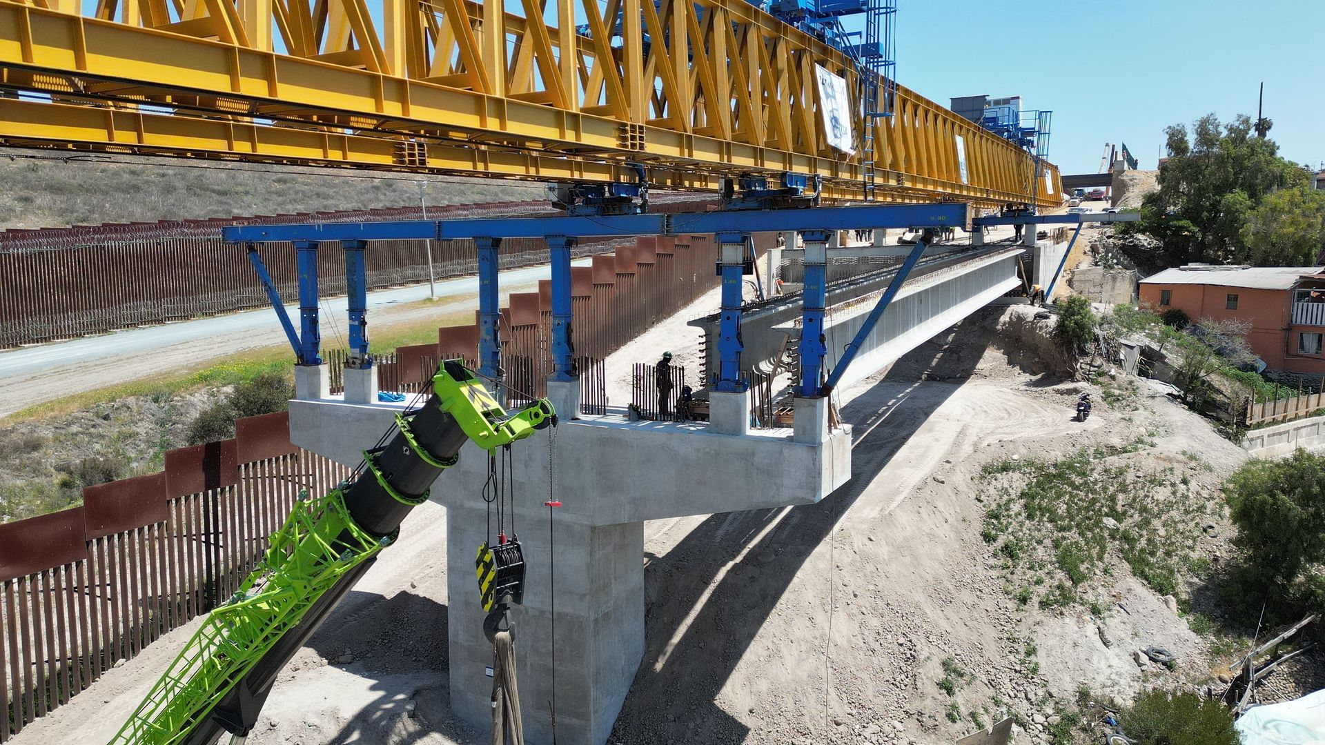 Construction of a bridge: yellow and blue machinery over a concrete structure, with a green crane in the foreground.