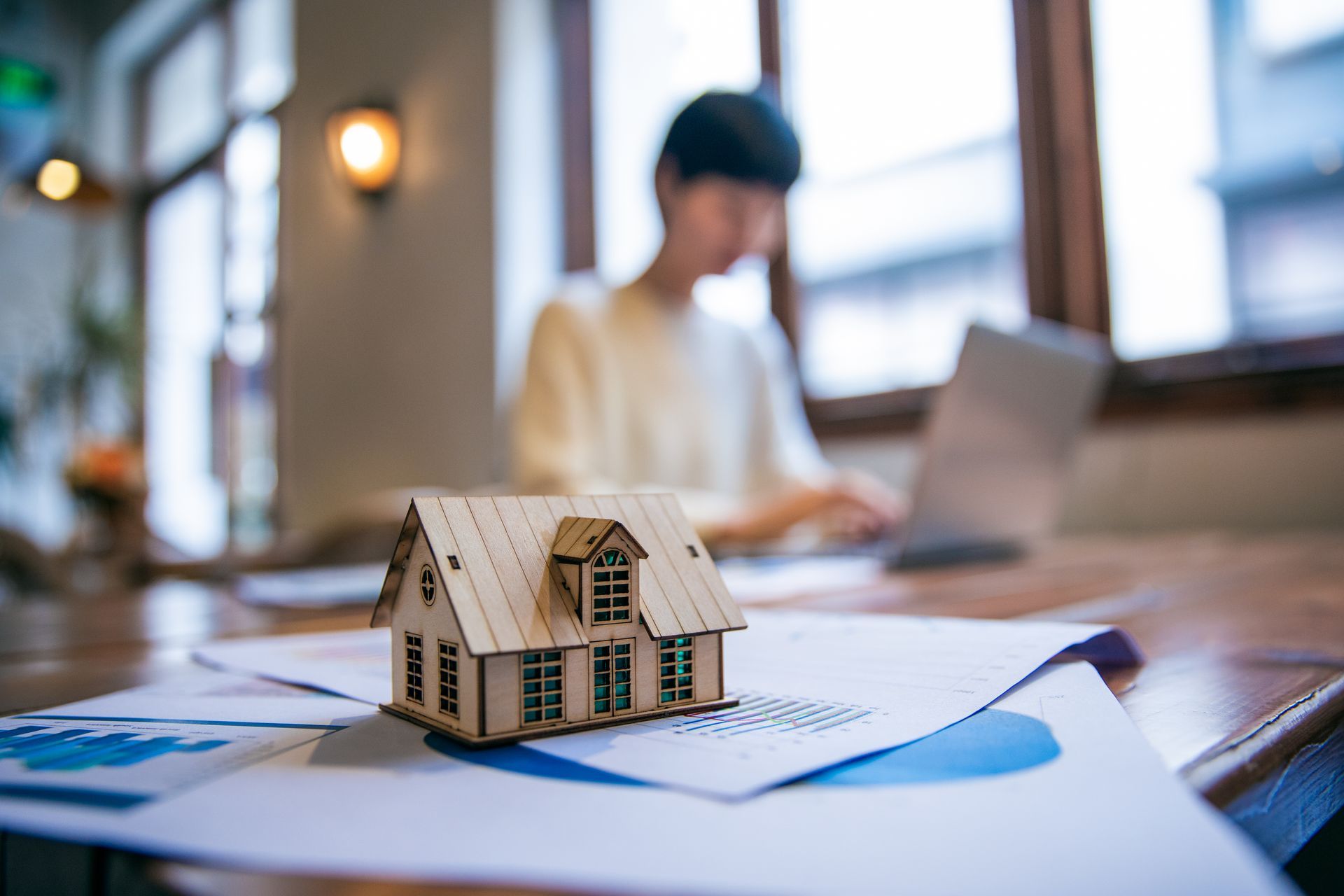 A model house is sitting on a table next to a man using a laptop.