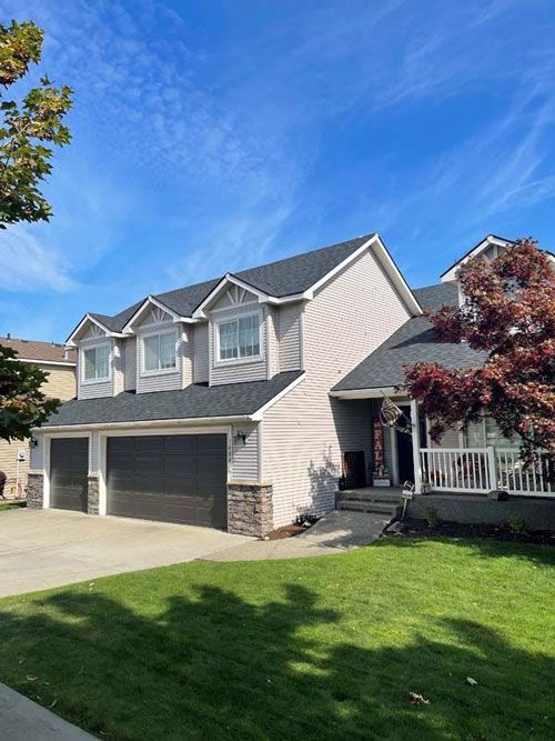 Two-story house with gray siding, dark roof, three-car garage, green lawn, and blue sky.