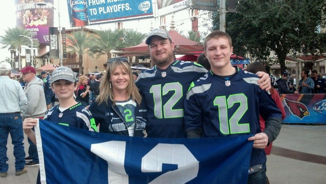 Family in Seahawks jerseys holding a 12 flag, smiling outdoors.