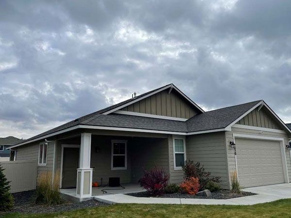 Green house with covered porch, garage, and cloudy sky.