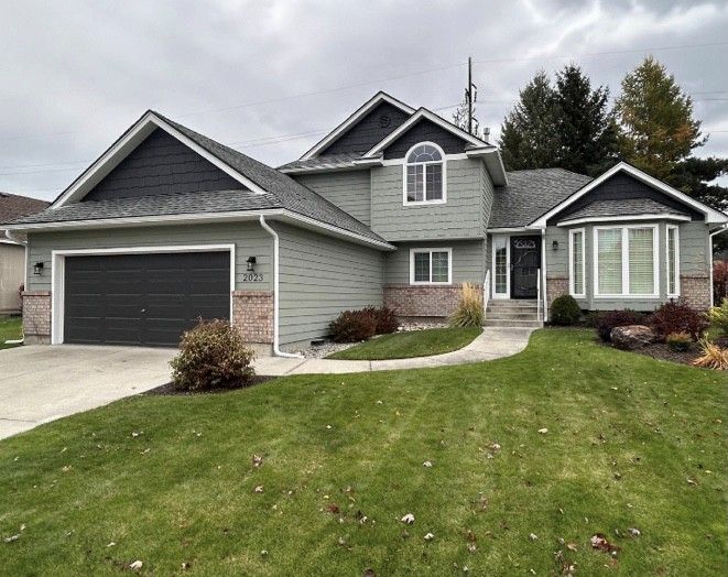 Suburban two-story gray house with attached garage and green lawn under overcast sky