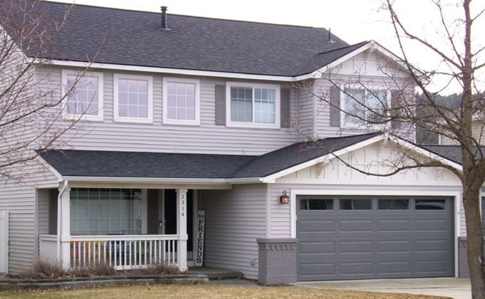 Two-story gray house with dark gray roof and garage door; small front porch.