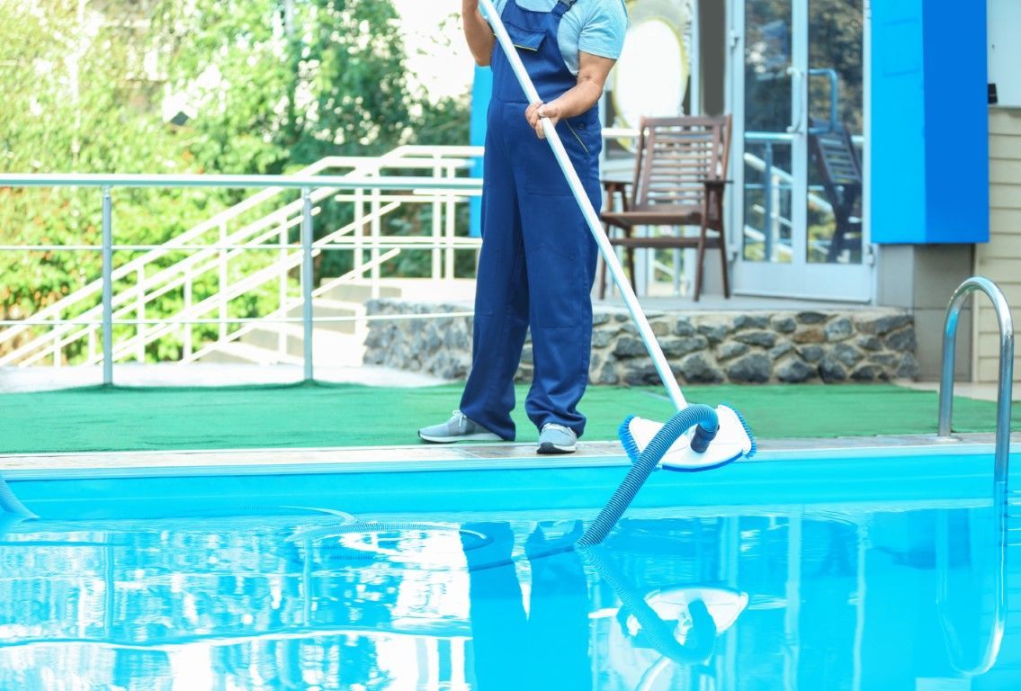 Person sweeping the pool deck beside a blue swimming pool