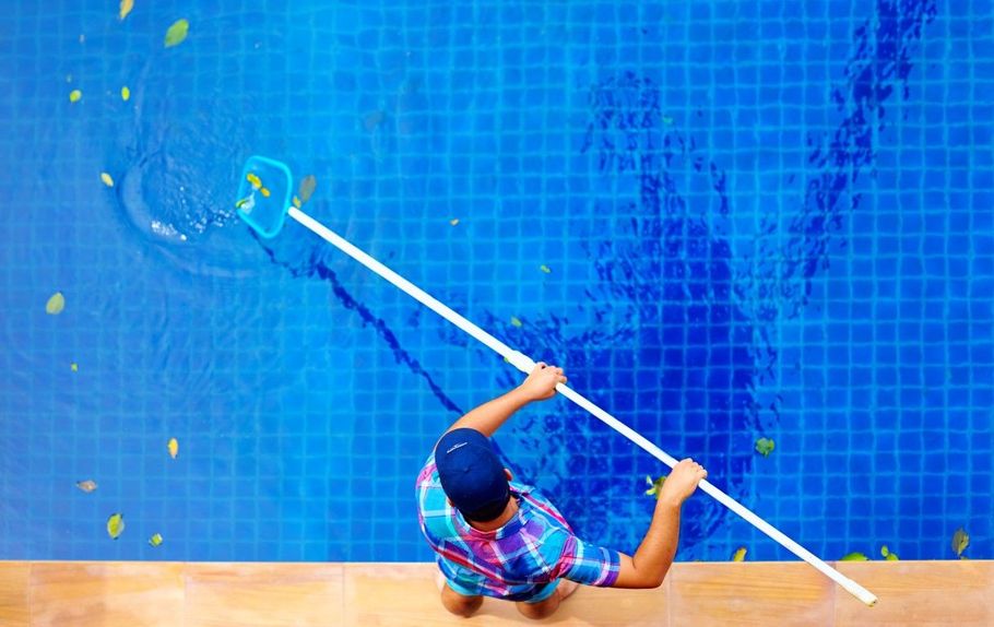 Person using a long pool pole in a bright blue tiled pool, seen from above