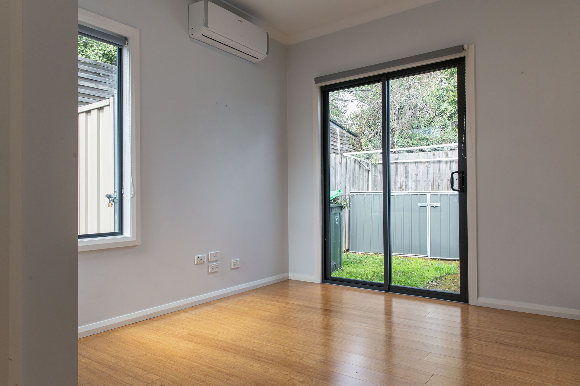 Empty room with a sliding glass door opening to a small fenced yard and wooden flooring.