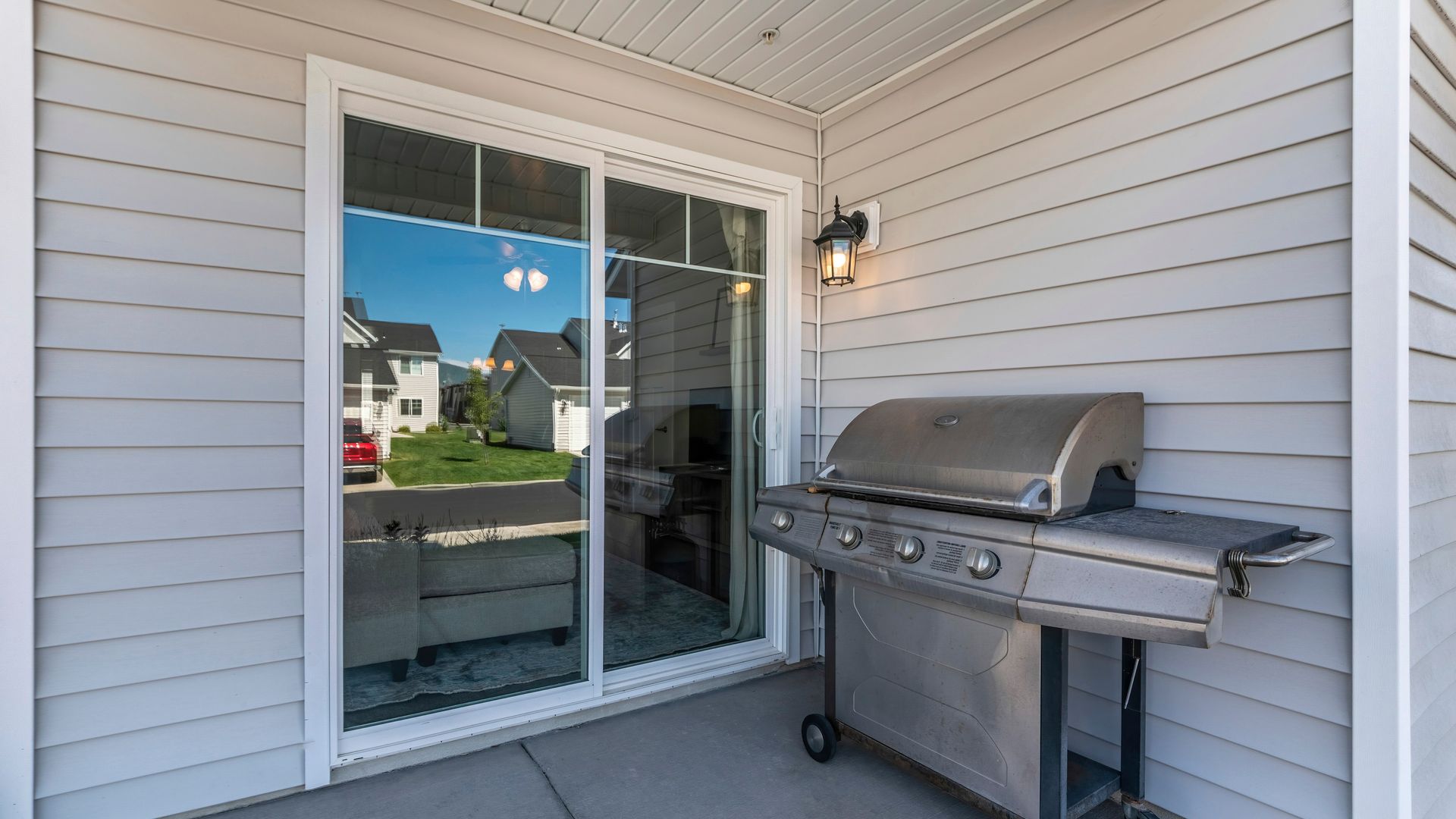 Sliding glass door leading to a patio with a grill and view of nearby homes outside.