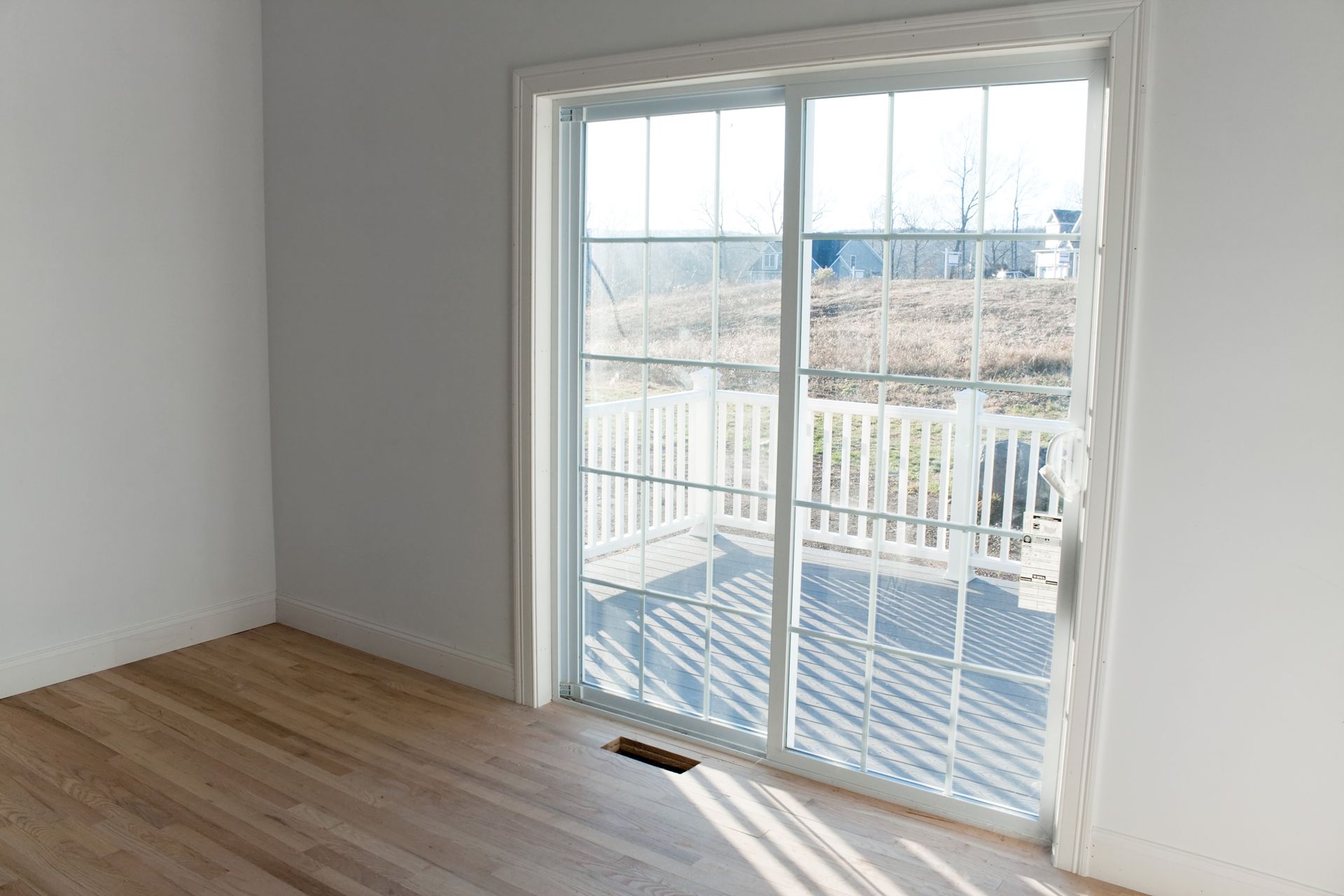 Sunlit room with a white sliding glass door leading to a wooden deck and open yard view. Sunlit room with a white sliding glass door leading to a wooden deck and open yard view.