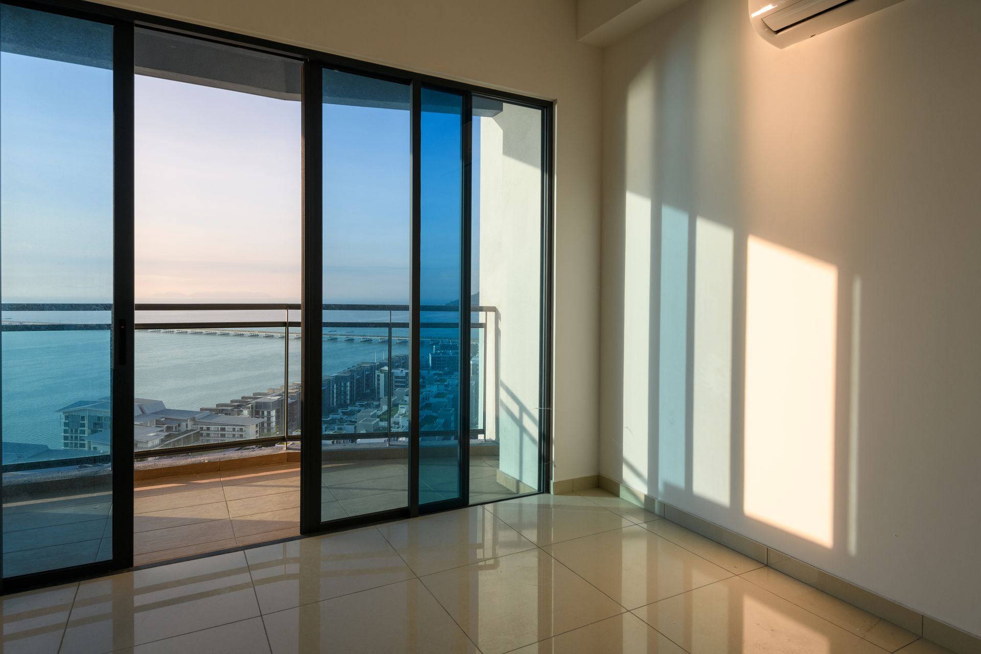 An empty room with sliding glass doors leading to a balcony overlooking the ocean.